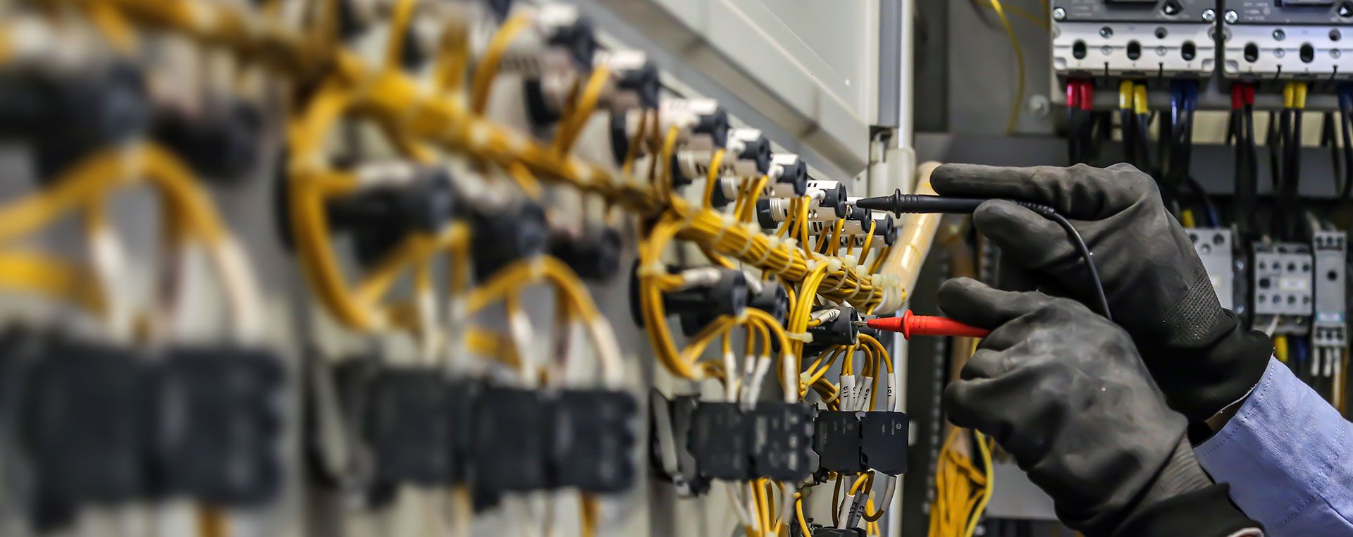 Ein elektronischer Schaltschrank an dem eine Person mit Schutzhandschuhen dran arbeitet und Messungen vornimmt