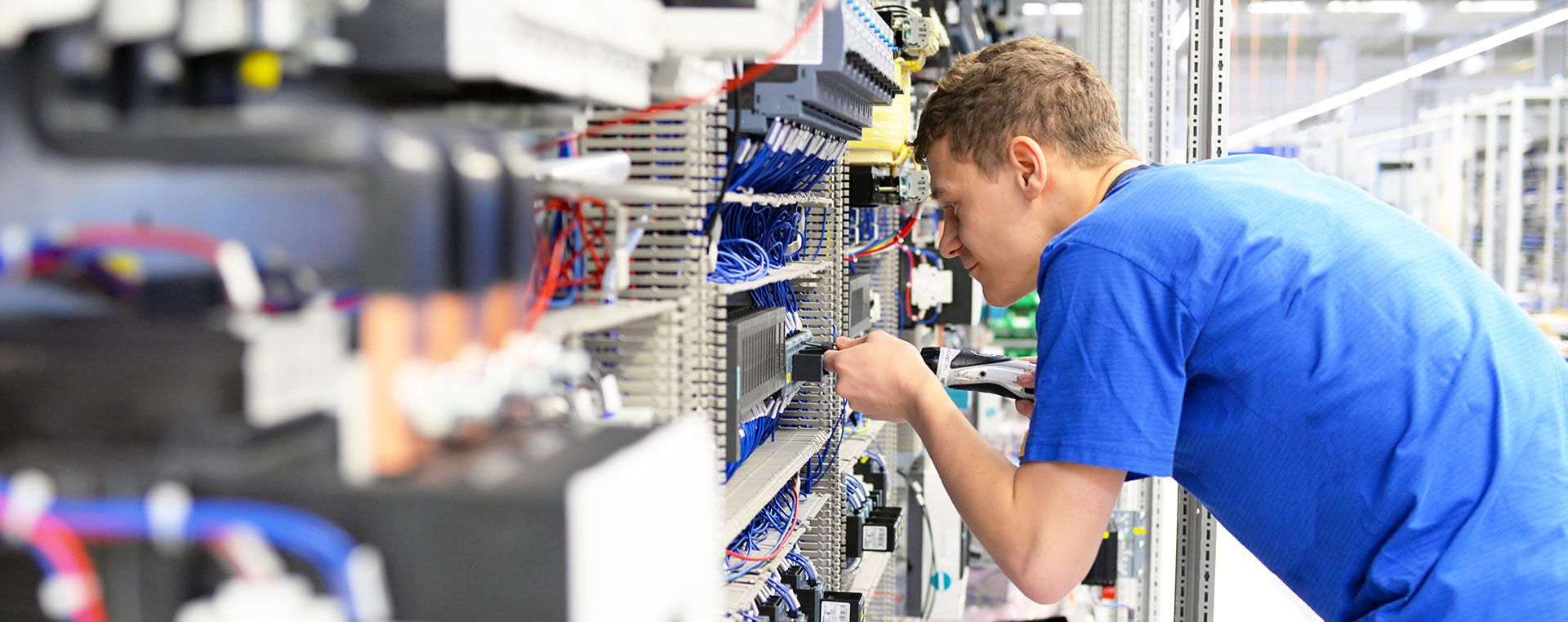 Ein Mann prüft die Anschlüsse in einem großem elektronischem Schaltschrank